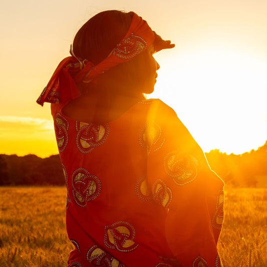 A woman wearing a red dress and red scarf looks off into the sunset.