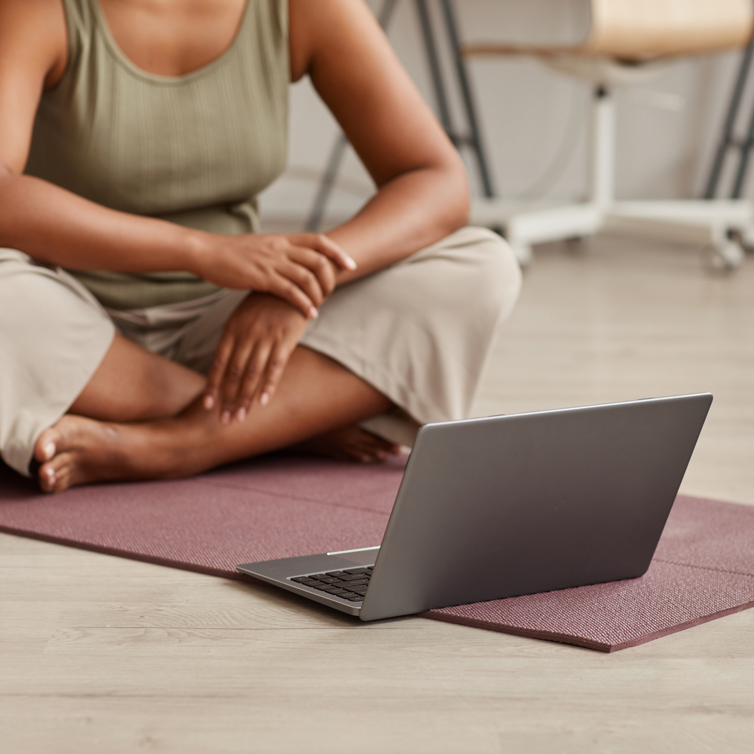 A photograph of a woman sitting on a yoga mat and looking at a laptop.