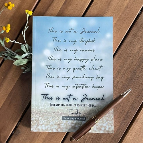 firefly journal, flat lay picture of light blue and gold book on a wood background with yellow flowers